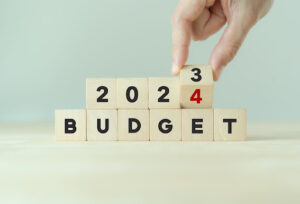 Hand flips a wooden cube and changes the inscription "BUDGET 2023" to "BUDGET 2024.”