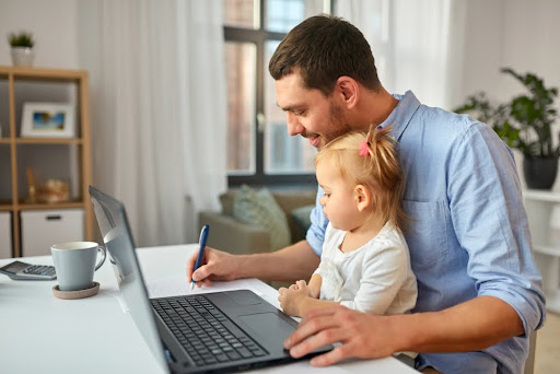 Employee working on computer from home with child on lap.